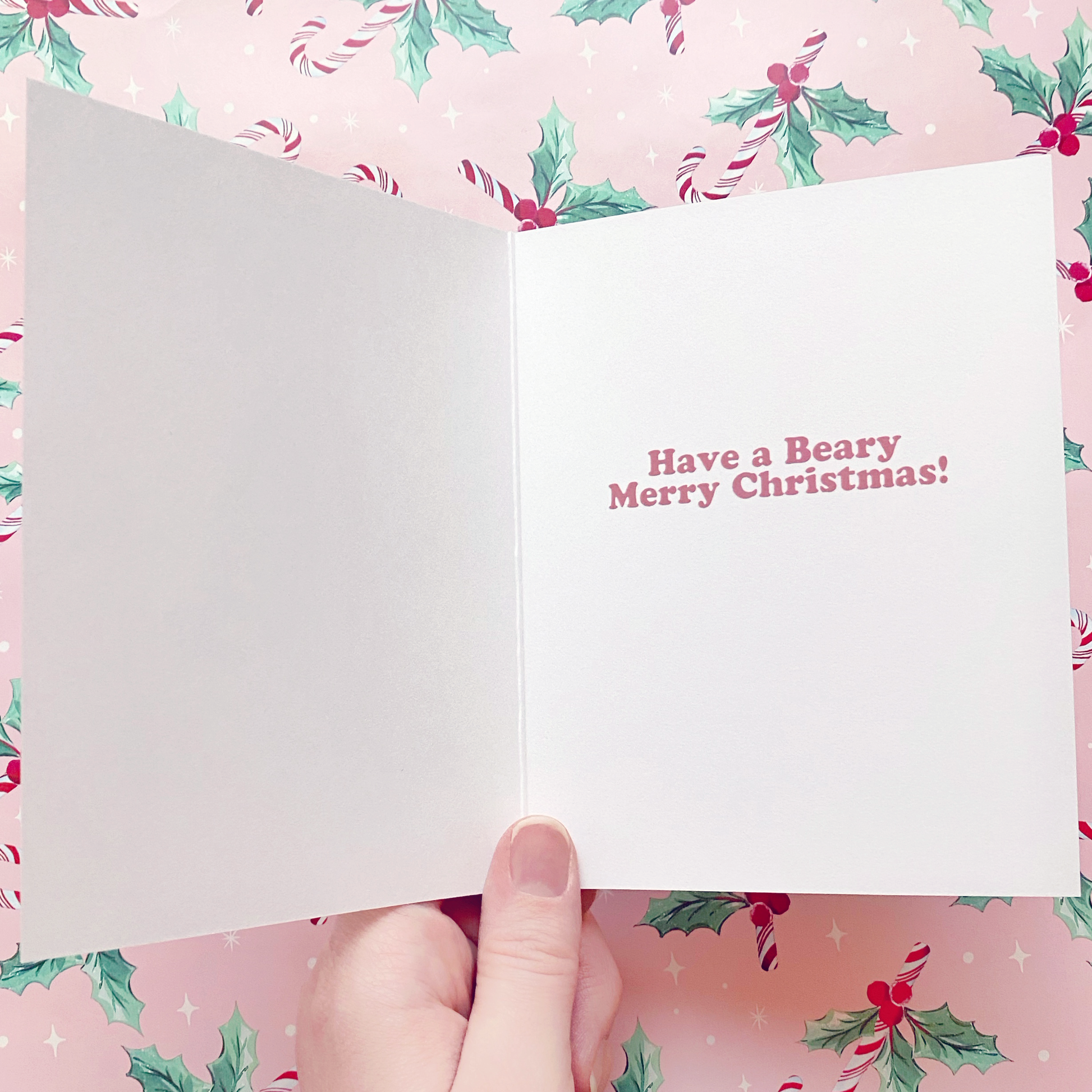 Inside of A2 Christmas card with the quote "Have a Beary Merry Christmas!" on the inside right side. Photographed on a pastel pink wrapping paper background with red and white candy canes and green and red bunches of holly.