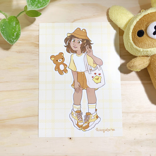 Printed illustration of a cute, tan skinned young girl wearing a yellow and white t-shirt, brown shorts, yellow and white tube socks, yellow white and brown sneakers, a brown bear bucket hat, a canvas tote bag with a cute yellow bird on it, and a floating teddy bear next to her. Photographed on a wooden background with a brown and yellow teddy bear to the right and a green plant at the top left for décor.